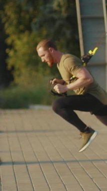 Sadık ve disiplinli bir adam TRX kayışlarını güzel bir açık hava ortamında güç eğitimi için kullanıyor.