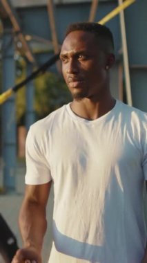 Beyaz gömlekli genç bir adam açık havada duruyor, yoğun atletizm antrenmanlarına hazır.