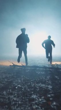 İki gölgeli figür, sisli, büyüleyici bir ormanda hızla koşuyor. Yumuşak, soluk ışıklarla aydınlatılıyor.