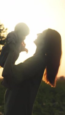 Sevgi dolu bir annenin huzur dolu bir siluet görüntüsü. Biricik çocuğunu göz kamaştırıcı bir gün batımı arka planına yaslıyor.