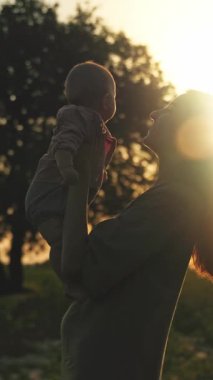 Sevgi dolu ve fedakar bir anne, güzel bir günbatımının sıcacık parıltısında güneşlenen kıymetli bebeğini neşeyle kucaklıyor.