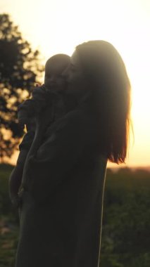 Bu huzurlu anda, sevgi dolu bir anne, gün batımının çarpıcı renkleriyle çerçevelenmiş kıymetli çocuğunu sıkıca kucaklıyor.