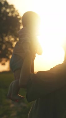 Sevgi dolu bir annenin güzel bir gün batımının keyfini çıkarırken nazikçe bebeğini kucağına aldığı yürek ısıtan bir siluet.