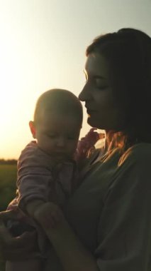 Sevgi dolu bir anne ve kıymetli bebeğinin çarpıcı bir günbatımı arkaplanına güzel bir şekilde çekildiği huzurlu bir an.