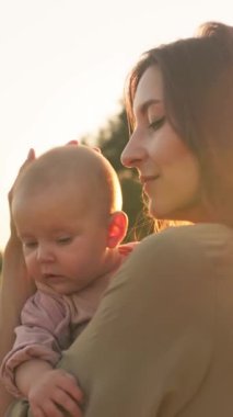 Sevgi dolu bir annenin güzel bir günbatımında değerli bebeğini nazikçe kucakladığı huzurlu ve rahatlatıcı bir an.