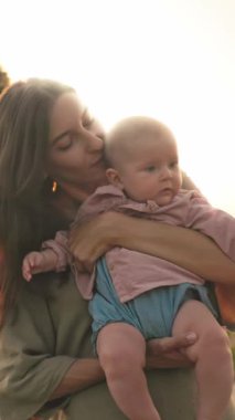 Güzel, doğal bir ortamda, sevgi dolu bir anne bebeğini nazikçe kucağına alır, saf sevgi ve sıcaklık saçar.