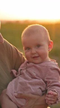 Yürek ısıtan bir an, güzel bir gün batımında şefkatli bir bakıcı tarafından nazikçe tutulan gülümseyen bir bebeği yakalar.