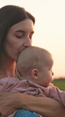 Sevgi dolu bir annenin, güzel bebeğini çarpıcı, canlı bir günbatımına karşı nazikçe tutması gibi hassas bir an yaşanıyor.