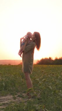 Sevgi dolu bir anne, güzel bebeğini güzel bir tarlada nefes kesici bir gün batımında nazikçe tutar.