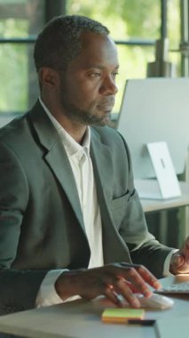 Odaklanmış ve takım elbise giymiş bir adam, çalışma masasındaki bilgisayarda özenle çalışıyor, doğal ışıkla aydınlatılıyor.