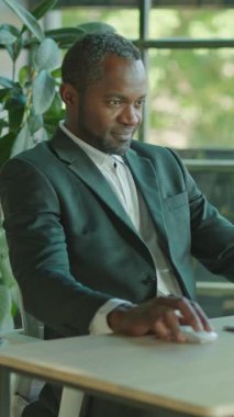 Özel dikim takım elbise giyen odaklanmış bir adam, bitkilerle dolu şık bir ofisteki bir masada özenle çalışıyor.