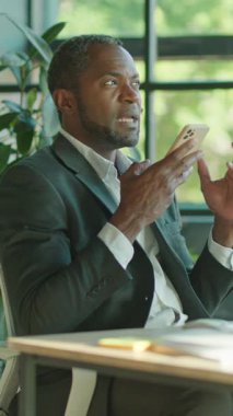 Parlak ve modern bir ofiste, şık takım elbiseli bir işadamı dikkatle akıllı telefonuna odaklanır.