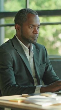 Takım elbise giymiş ciddi ve odaklanmış bir işadamı, modern ofis alanındaki bir masada özenle çalışıyor.