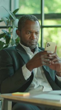 Yüksek odaklı bir işadamı, çağdaş ve şık bir ofis ortamındayken akıllı telefon kullanıyor.