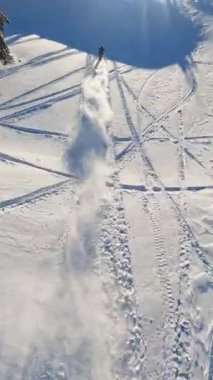 Hava görüntüsü, parlak güneş ışığıyla aydınlatılan kayak pistleri ve kar motosikletli patikalarla karlı bir araziyi ortaya çıkarıyor.