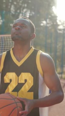 Son derece odaklanmış ve kararlı bir basketbol oyuncusu sahadaki parlak güneş ışığı altında ustalıkla topu sürüyor.