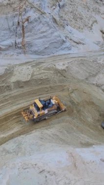 Bir buldozer, çeşitli toprak malzemeleriyle çevrili işlek bir inşaat sahasında dengesiz bir arazide çalışıyor.