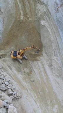Bir inşaat sahasında kumlu bir yüzey üzerinde çalışan bir kazıcı, iş başında ağır makineler gösteriyor..