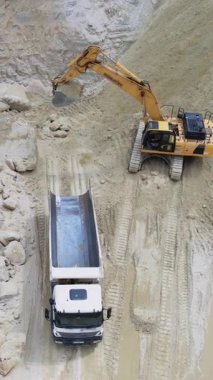 Yoğun bir inşaat alanında, bir kazıcı büyük bir çöp kamyonuna çeşitli materyalleri özenle yüklüyor.