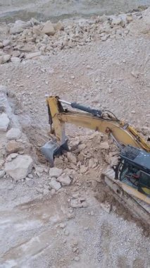 İnşaat alanında çakıl ve toprağı kazan kazıcı, iş başında ağır makineler gösteriyor..