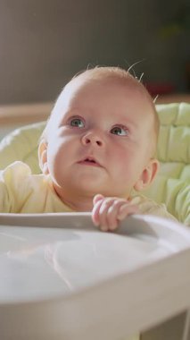 Yüksek bir sandalyede oturan meraklı bir bebek minicik elleriyle uzanır, masumiyetini ve saf merakını gösterir.