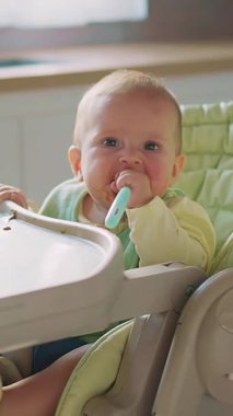 Neşeli ve neşeli bir bebek yüksek bir sandalyede oturur, yemek saatinde bir kaşığa uzanmaya can atar.