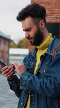 Şık bir genç adam hareketli sokaklarda akıllı telefonuyla aktif olarak modern şehir modasını sergiliyor.