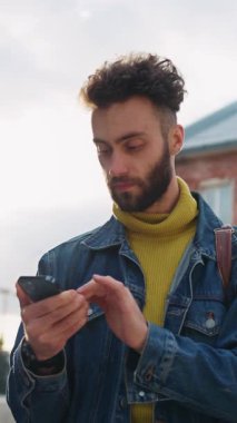 Modayı takip eden genç bir adam canlı modern şehir ortamında akıllı telefonuyla canlı bir etkileşim içindedir.