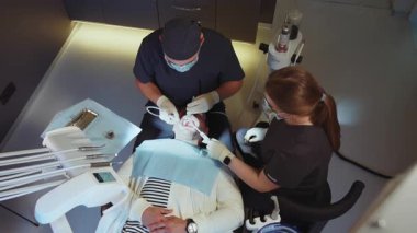 Tıbbi klinikte dişçi, tıbbi maskeli asistan diş tedavisi için diş aletleri tutuyor. Hydience ve sağlıklı.