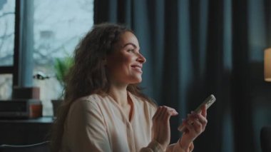 Kendine güvenen beyaz bir kadının elinde cep telefonuyla partneriyle mesajlaştığı yatay bir çekim. Zarif kıyafetli güzel bir kız içeride sohbet ediyor. Dijital teknoloji