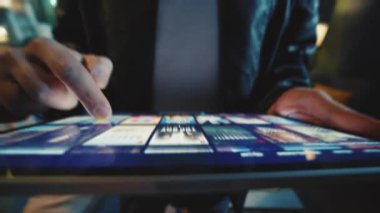 Dijital tabletin yakın çekim görüntüleri erkeklerin elinde. Deri ceketli tanınmayan genç adam, yayın platformunu kullanıyor, uygulamayı kaydırıyor ve izlemek için film seçiyor. İçeride. Eğlence