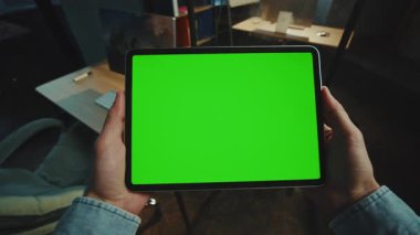 Karanlık ofiste elinde yeşil ekranlı bir tablet bilgisayarı tutan bir adam. Model ekran. Cihaz. Daire