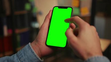 Kot ceketli erkeklerin elinde yeşil ekranlı akıllı telefon çekimleri. Adam sosyal medyayı tarıyor, cihazdan mesaj okuyor. Krom anahtar. İçeride. Oturma odasının arka planı bulanık. İyi akşamlar.