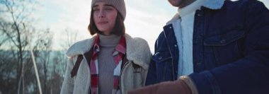 Kış ormanında el ele tutuşup sohbet eden mutlu çiftin görüntüsü. Güneşli bir günde kadın ve erkek hafta sonunun tadını çıkarıyorlar. Güneş ışığı