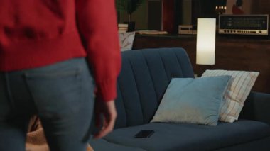 Kot pantolon ve mercan kazak giyen zayıf genç bir kadının akıllı telefon alıp koltuğa oturduğu bir sahne. Sevimli gülümseyen beyaz kız kanepede dinleniyor. Alet ekranına bakıyor.