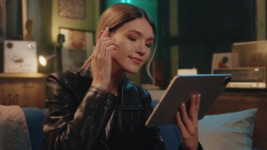 Güzel, genç, beyaz saçlı, at kuyruklu bir kadın. Tablet ekranına bakıyor ve rahat, modern oturma odasında neon ışıklı bir kanepede otururken daktilo yazıyor. Alet kullanarak gülümseyen kız. Dinlen.