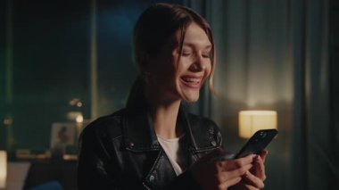 Güzel beyaz gülüşlü hoş görünümlü genç bir kadının karanlık odada neon ışıklarla sohbet edişinin görüntüsü. Deri ceketli güveni tam bir kız, alet kullanıyor. Randevu uygulaması konsepti. Kapalı