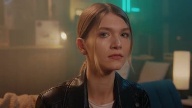 Burnunda yüzükler olan ve evdeki kanepede oturan genç bir kadının ciddi yüzü. Gece lambası