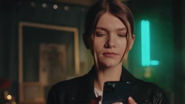 Ciddi sarışın genç bir kadın modern odada kendine güvenen akıllı telefon kullanıyor. Gece lambası