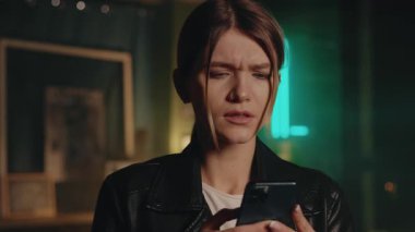 Güzel genç bir kadın ayakta durup akıllı telefon kullanıyor modern odada mutlu ve gülümsüyor. Gece lambası