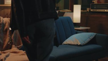 Mavi bir kanepede oturan gülümseyen sarışın genç bir kadın akıllı telefon kullanarak modern odada mutlu hisseder. Gece lambası