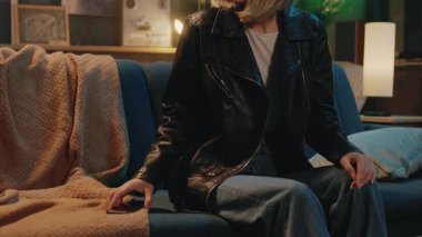 Mavi bir kanepede oturan üzgün sarışın genç kadın akıllı telefon kullanarak modern odada yorgun ve baş ağrısı çekiyor. Gergin.