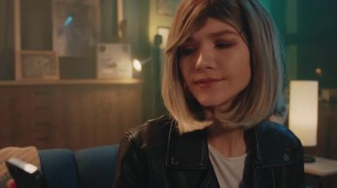 Mavi bir kanepede oturan çekici sarışın genç kadın akıllı telefon kullanarak modern odada üzgün hissediyor. Gergin.