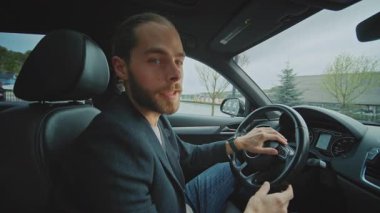 Arabanın içindeki kameraya bakarak konuşan ve gülümseyen genç bir adamın portresi. Kendine güven.