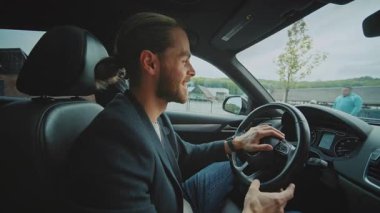 Araba süren, konuşan ve gülümseyen bir adam arabanın içindeki kameraya bakıyor. Kendine güven.