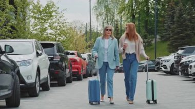 Gündüz vakti, güzel modern otelin önünde arabalarıyla otoparkta yürüyen bavullu iki zarif kadın. Gri saçlı anne ve güneş gözlüklü yetişkin kız konuşuyor. Hafta sonu. Yaşam tarzı. Açık havada.