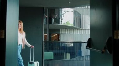 Modern otel koridorunda bavullu sarışın bir kadınla zarif giyinmiş mutlu genç bir iş kadını fotoğrafı. Güzel ve muhteşem bir iç mekan. Tatil köyü kavramı. Hafta sonları