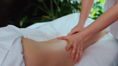 Masaj masasında yatan beyaz bir kadının görüntüsü. Sakin ve sakin bir atmosferde müşterinin bacaklarına masaj yapan bir kadın. Spa merkezi. Terapi konsepti. Kapalı