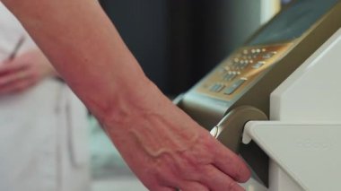 Kafkasyalı orta yaşlı bir kadının spa merkezindeki sağlık muayenesi sırasında elinde tıbbi aletle görüntüsü. Kot pantolonlu, tanınmayacak kadar olgun bir kadının fotoğrafı. Gündüz vakti. Kapalı