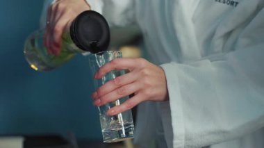 Beyaz bornozlu kadın elleri bardaklara su dolduruyor. Kaplıcadaki spada sağlık içecekleri. Sıvı ve sağlık. Sağlık programı ve diyet